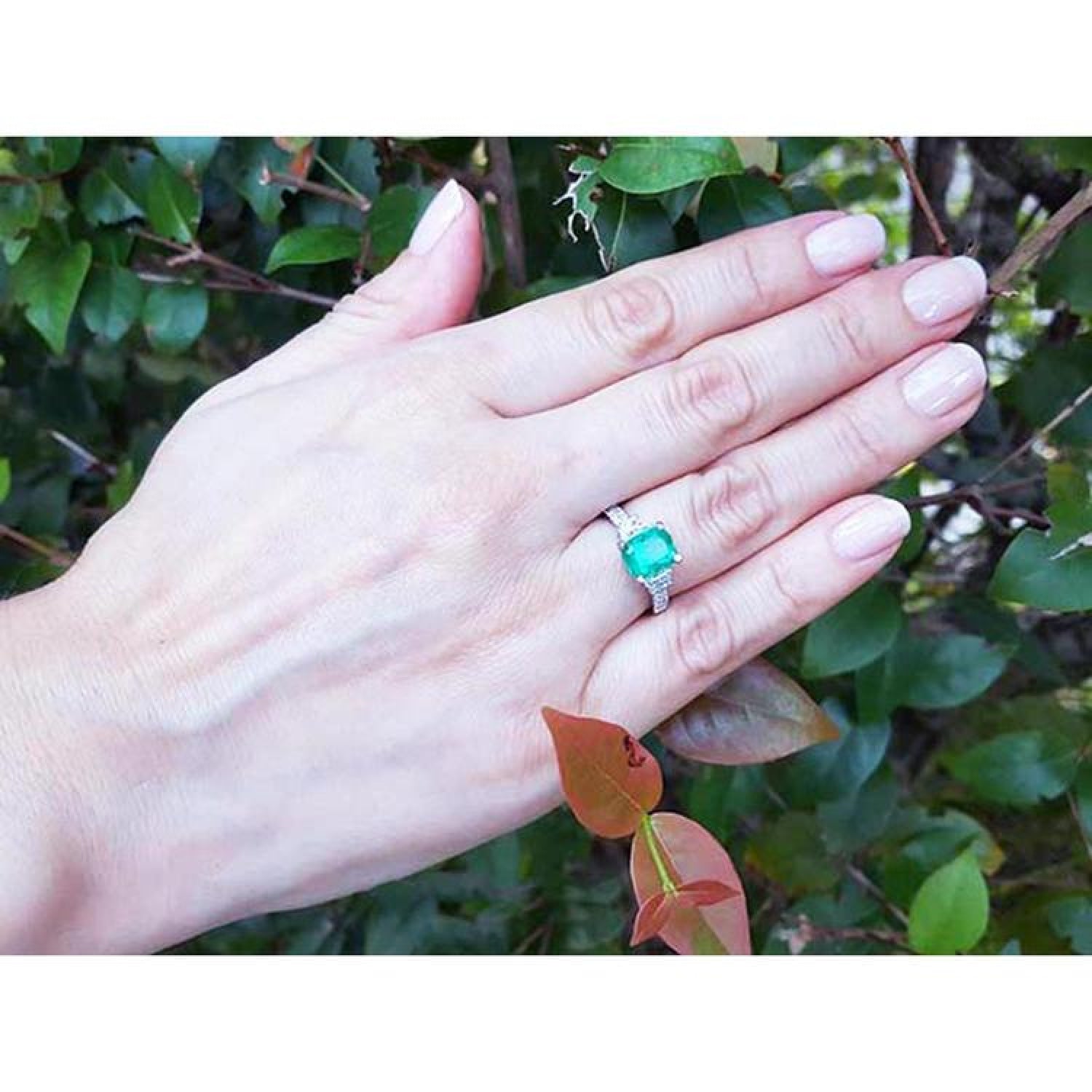 18K white gold ring with a cushion-cut emerald and trapezoid side diamonds on a hand.