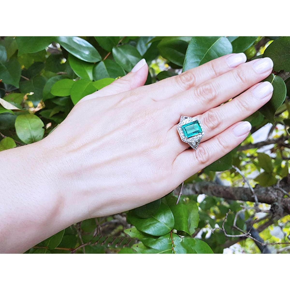Hand wearing a Ladies' natural Colombian emerald ring crafted in 18k white gold against a green leafy background.