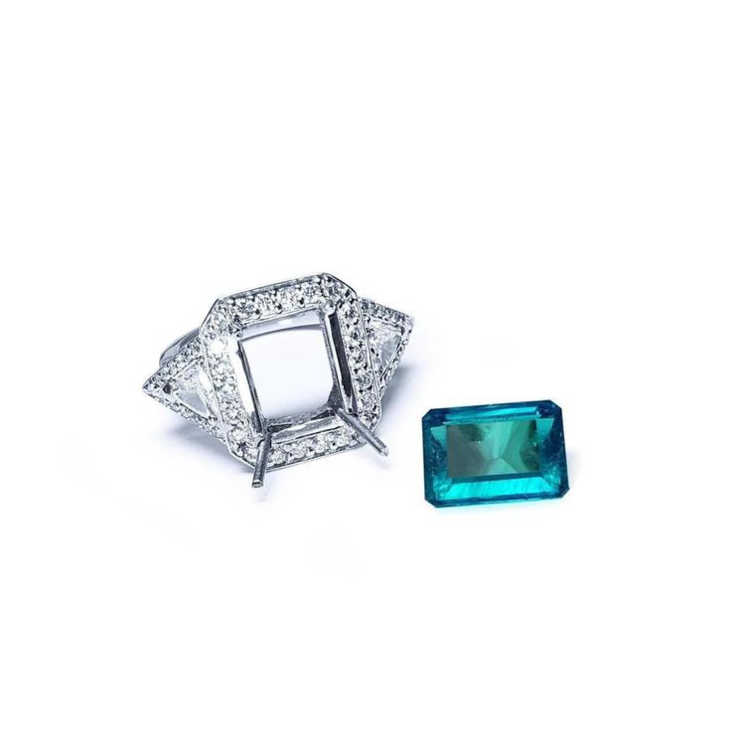 18K white gold diamond halo ring setting with trillion sides next to a loose rectangular emerald.