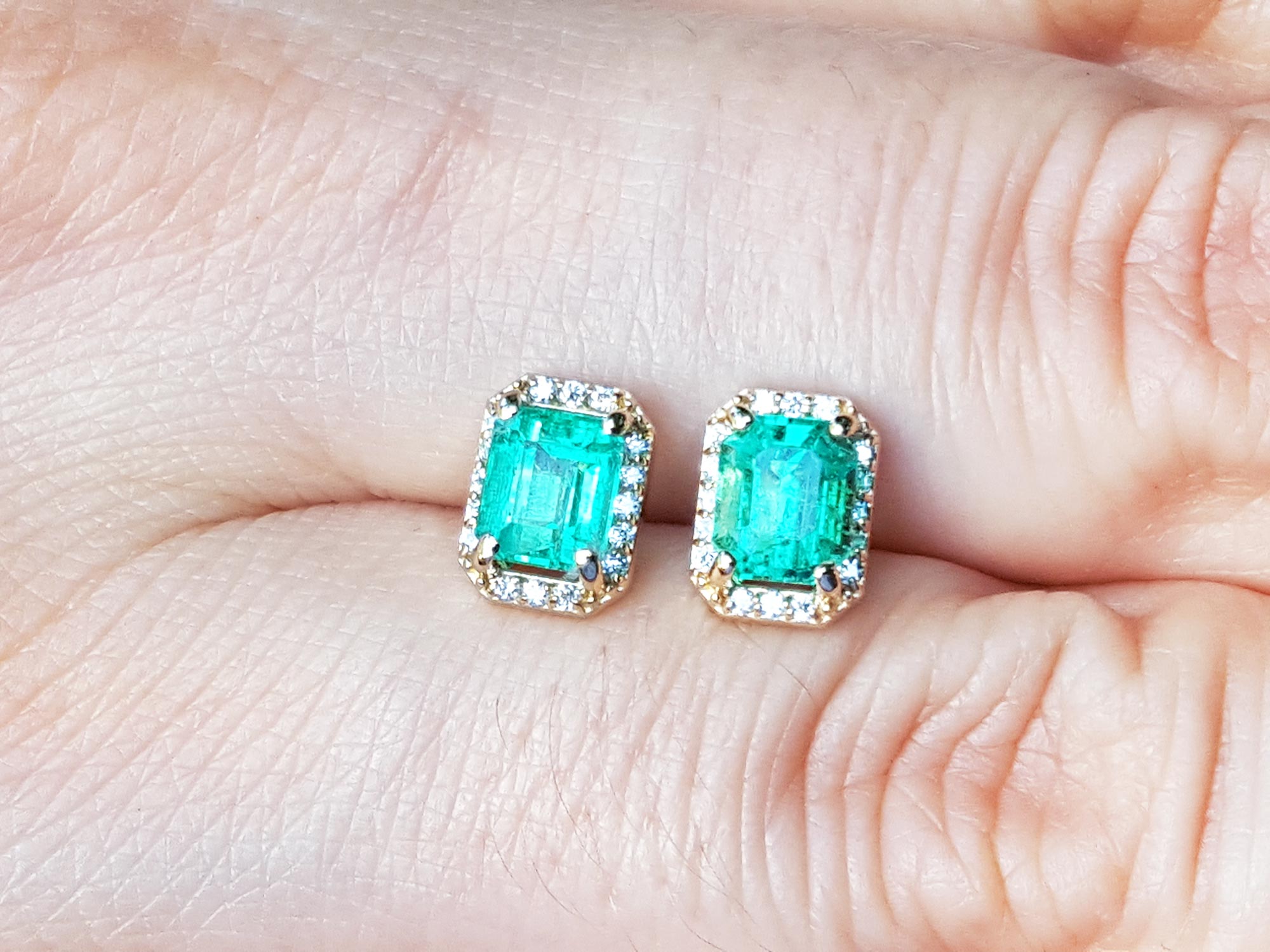 Emerald green gemstone earrings held between fingers.