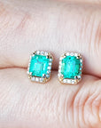 Emerald green gemstone earrings held between fingers.