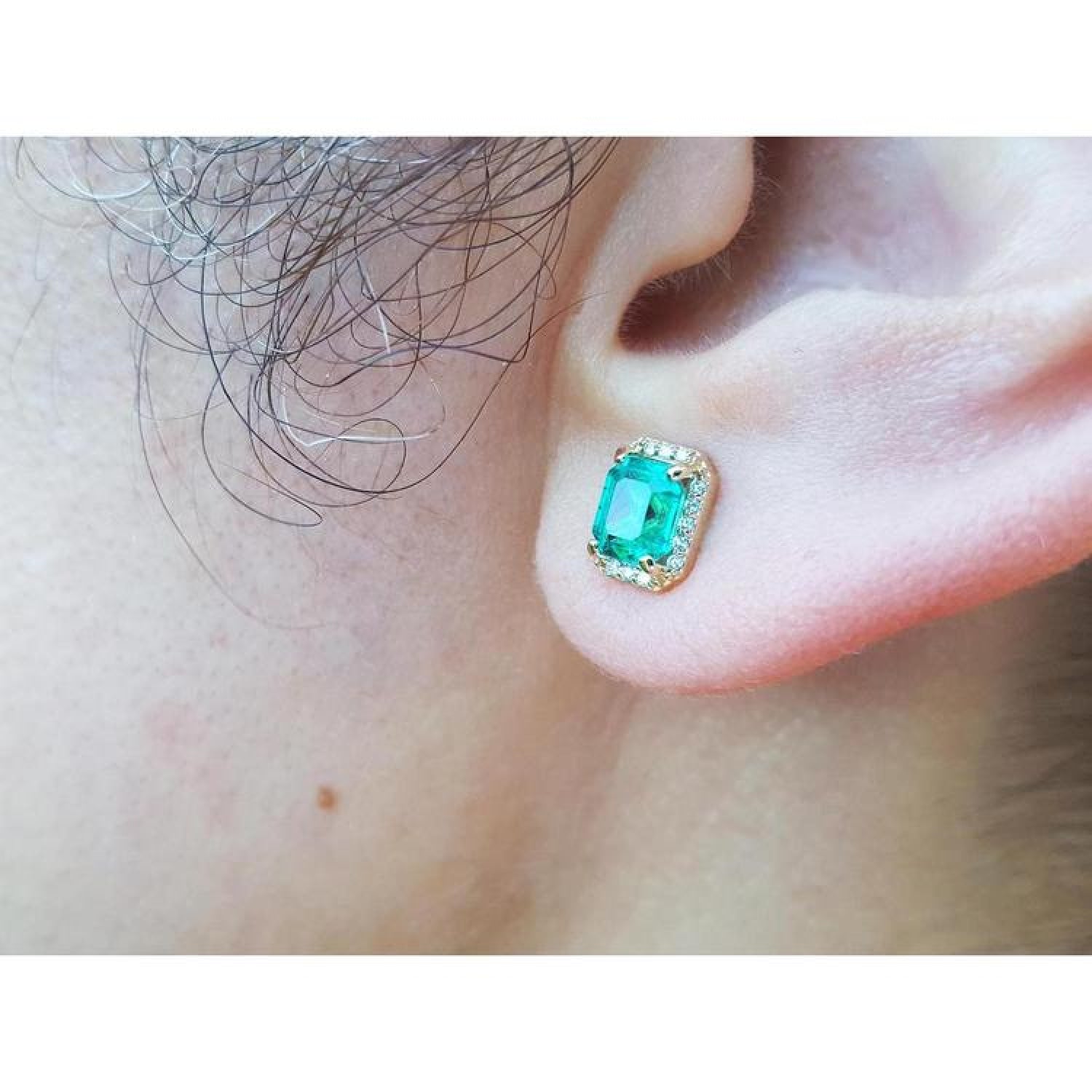 Colombian emerald halo stud earring with diamonds in 14k yellow gold on an ear.