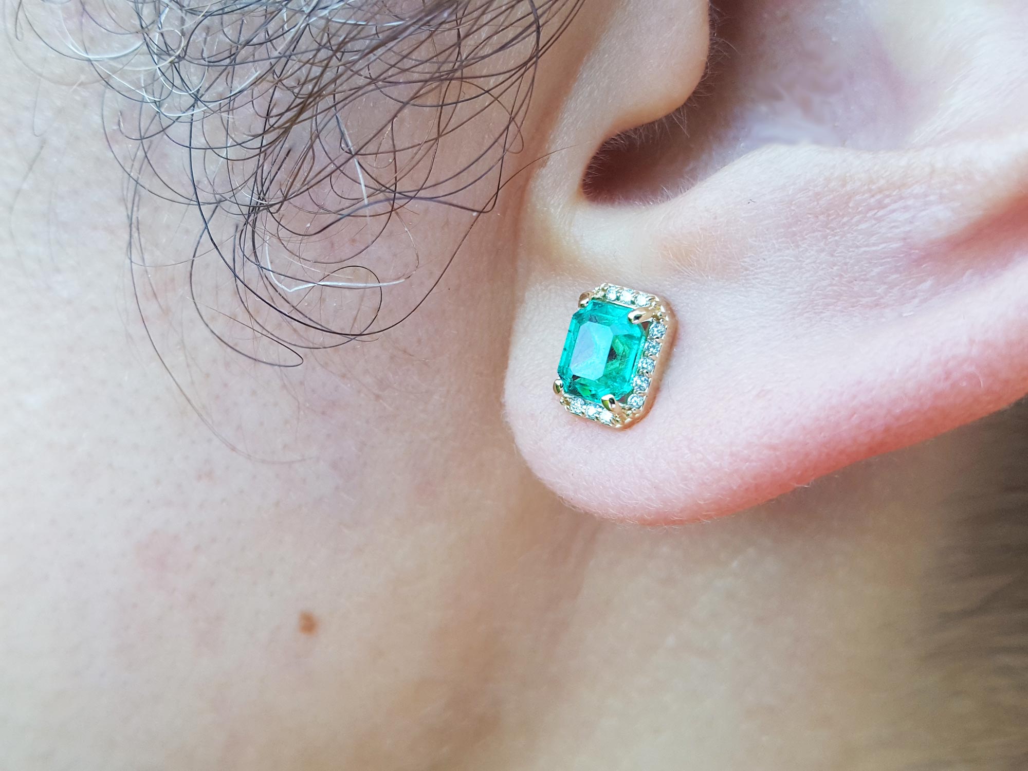 Close-up of an ear wearing emerald stud earring.