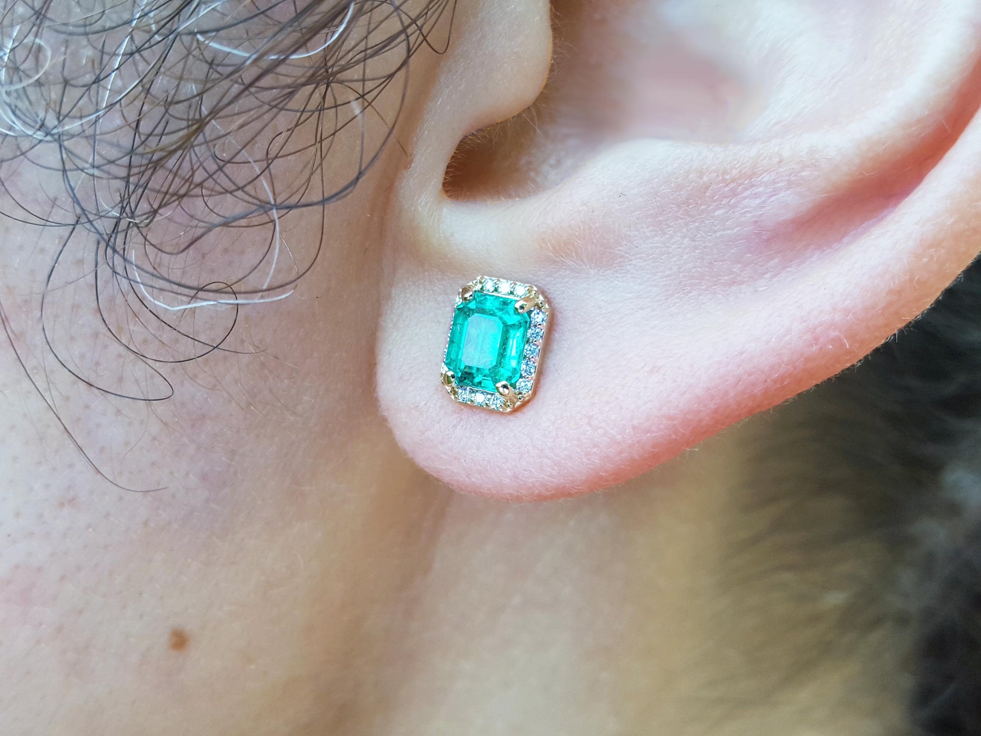 Close-up of an ear wearing a natural emerald stud earring.