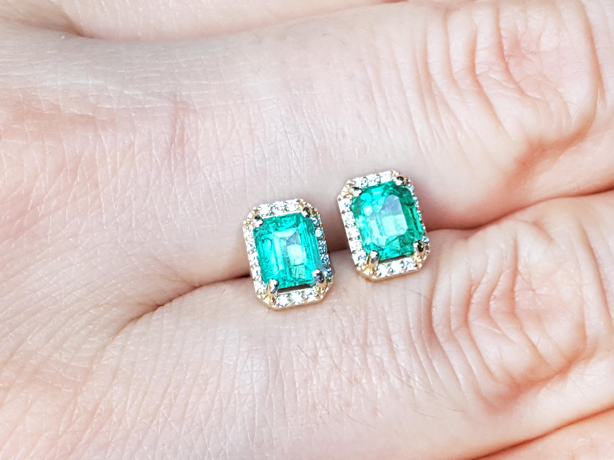 Emerald green gemstone earrings placed between fingers.