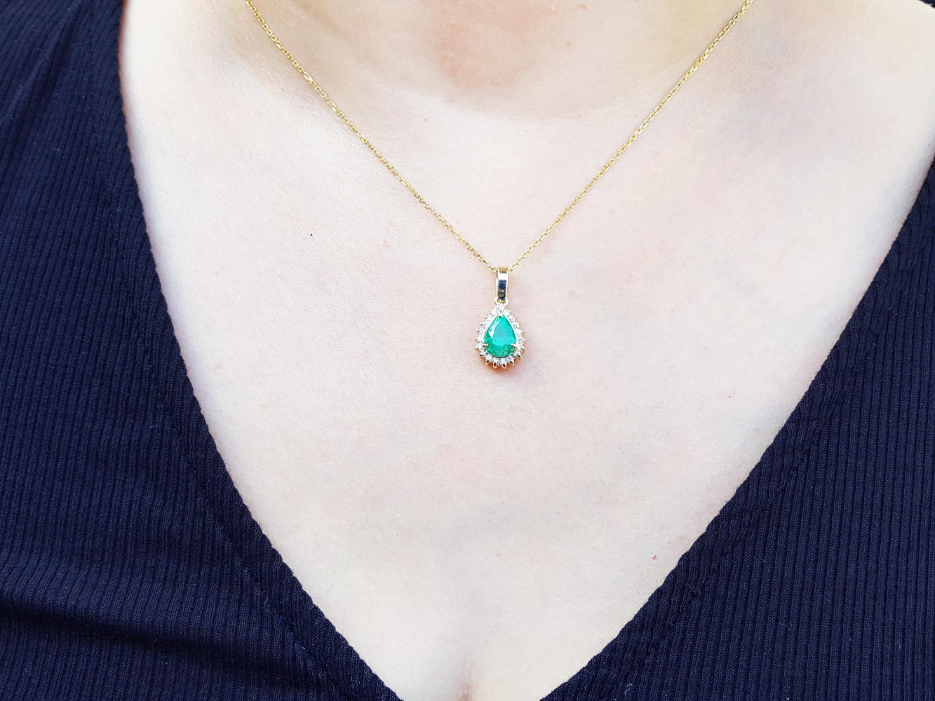 Gold necklace with a green teardrop emerald pendant on a woman wearing a dark blue top.