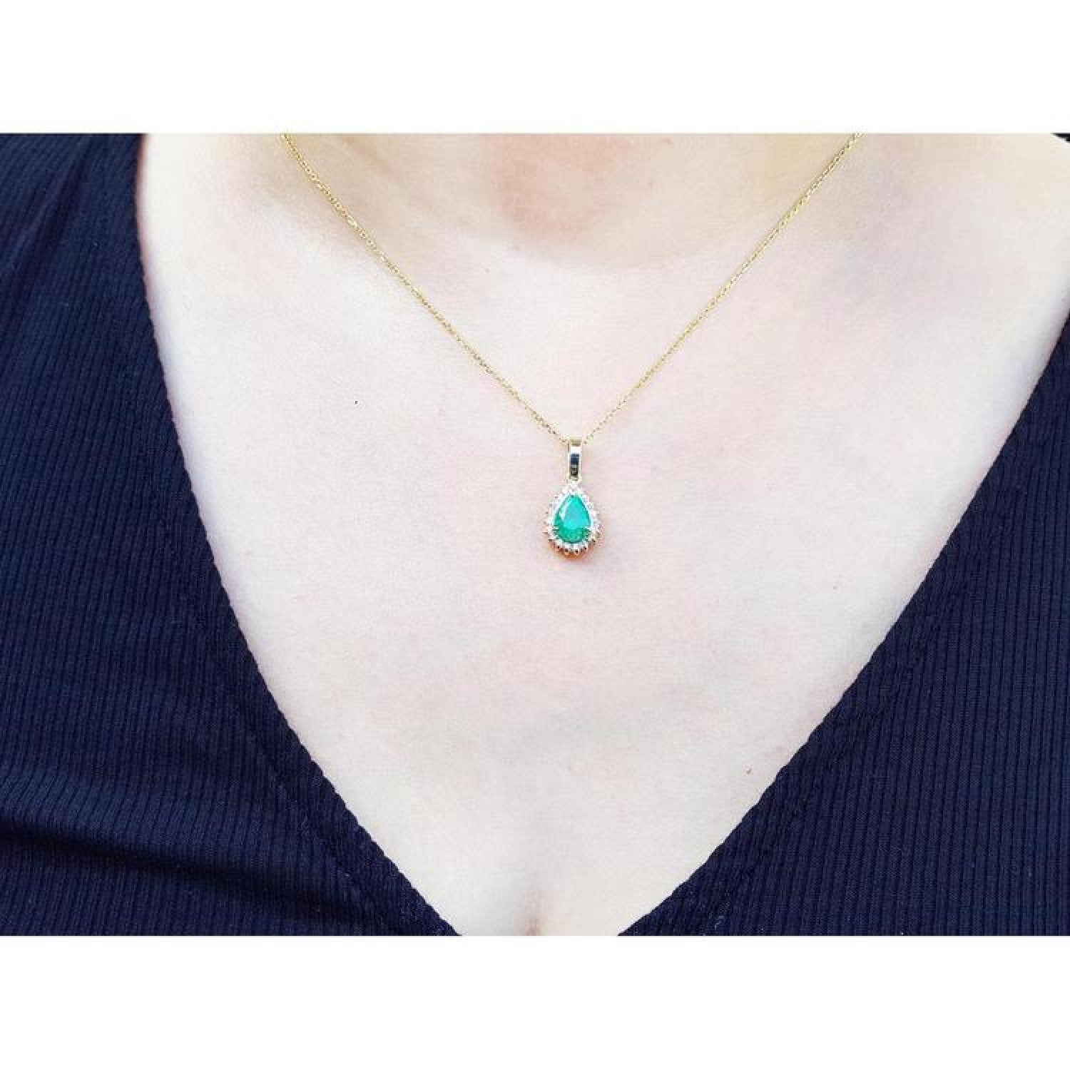 Pear-shaped Colombian emerald pendant with halo diamonds on a 14K yellow gold chain, worn on a person.
