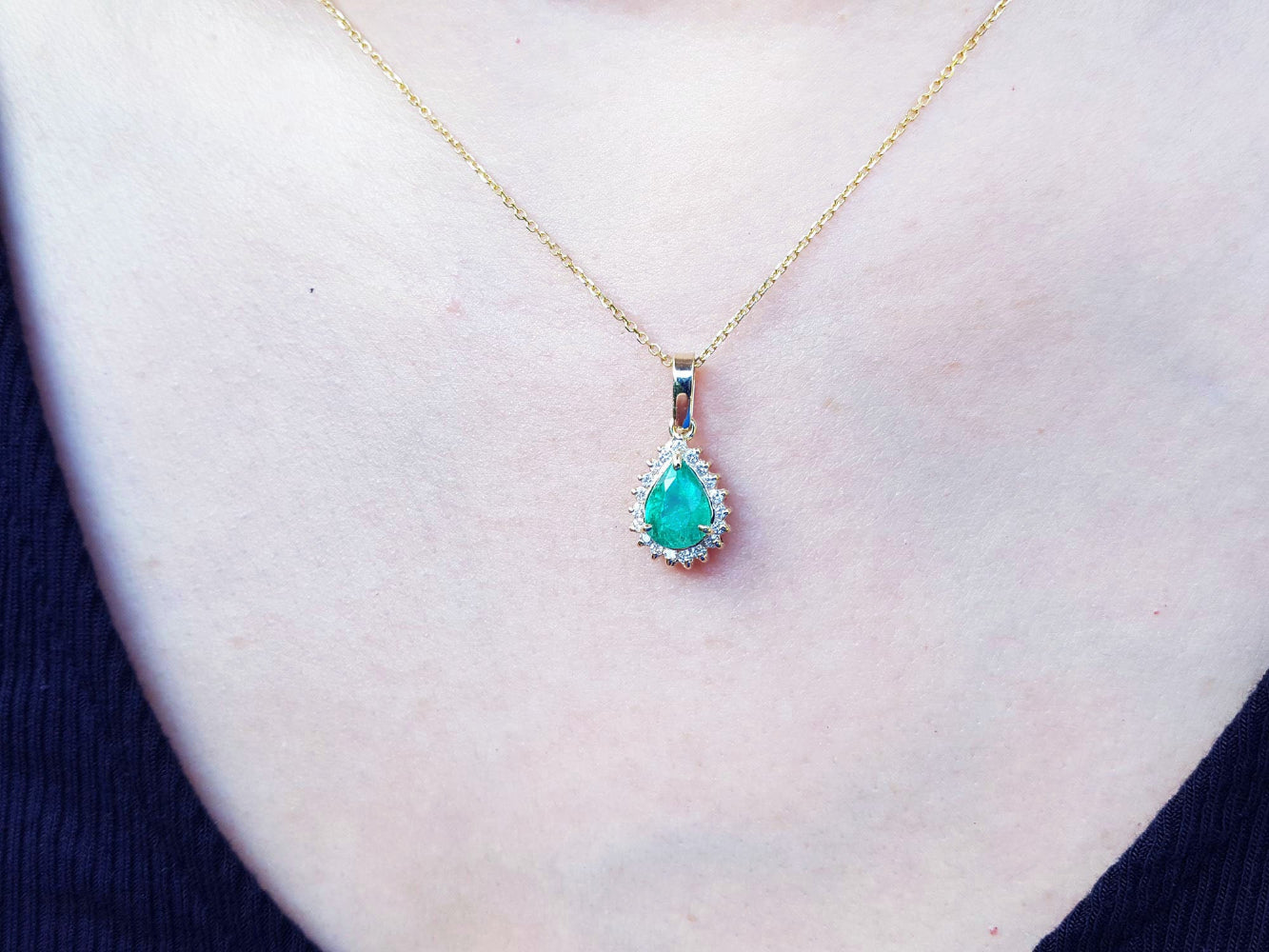 Gold necklace with a natural colombian teardrop emerald pendant on a person&#39;s neck.