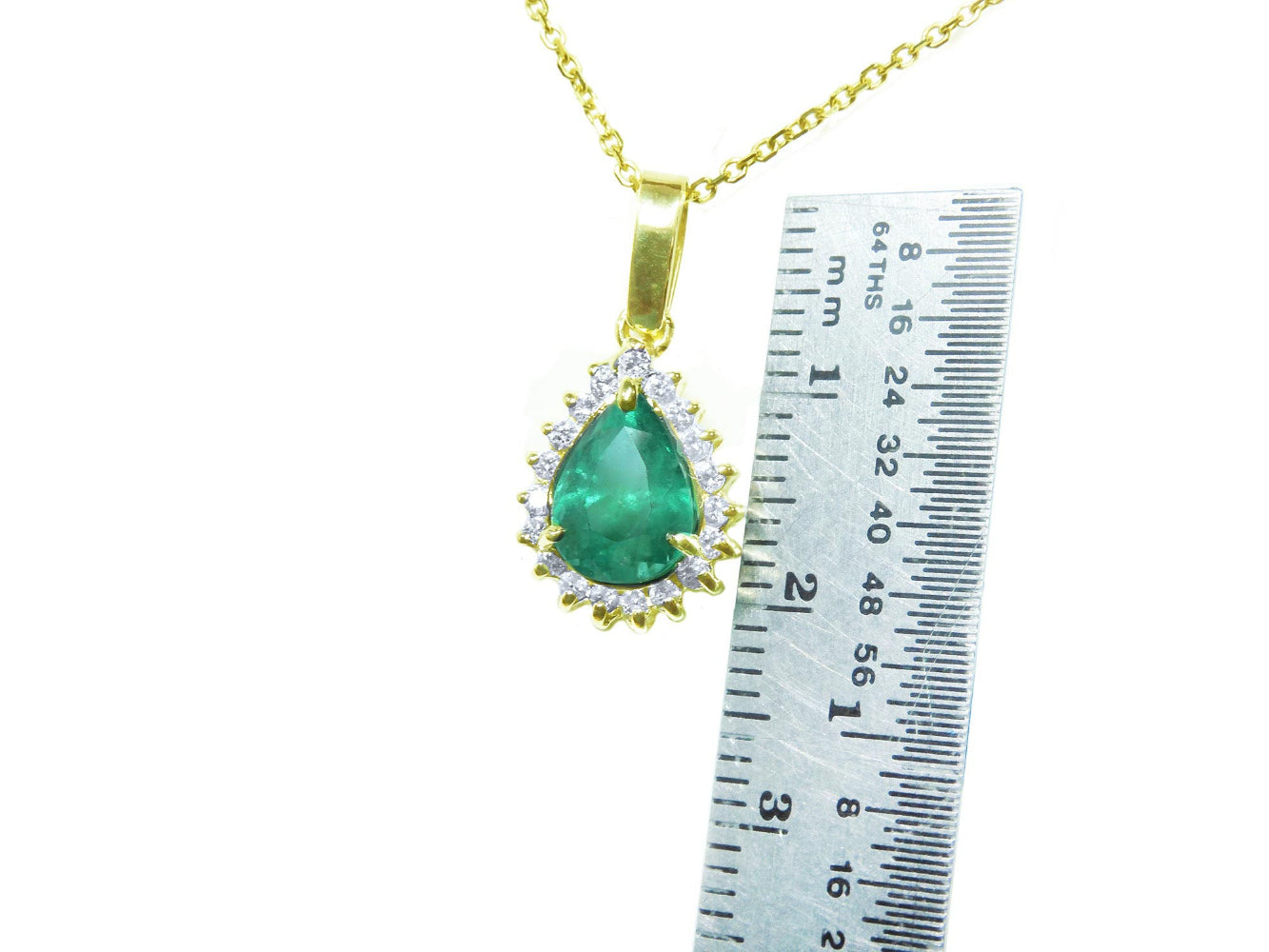 Gold necklace with a natural teardrop emerald pendant next to a ruler for scale on a white background.