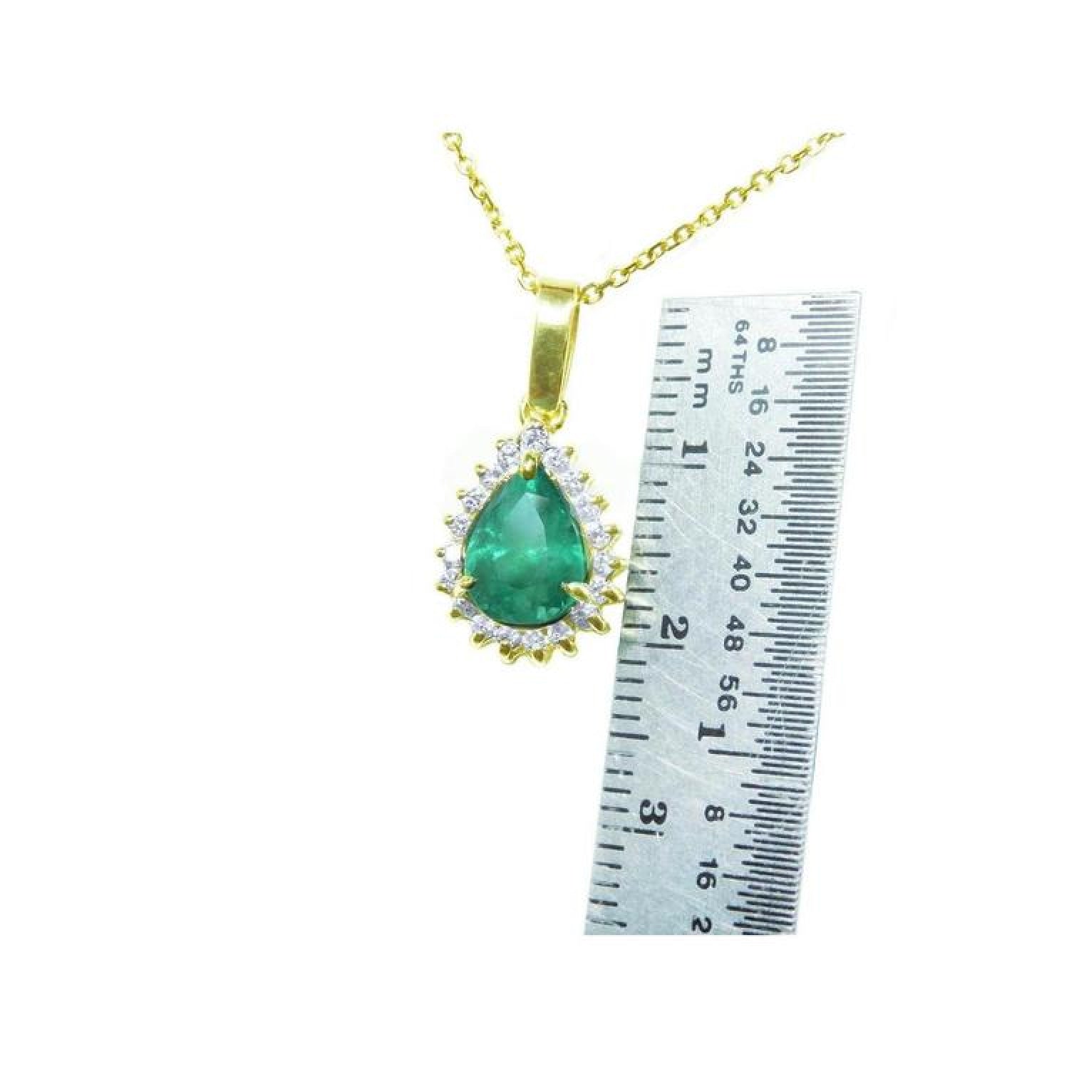 Pear-shaped Colombian emerald pendant with halo diamonds in 14K yellow gold, next to a ruler.