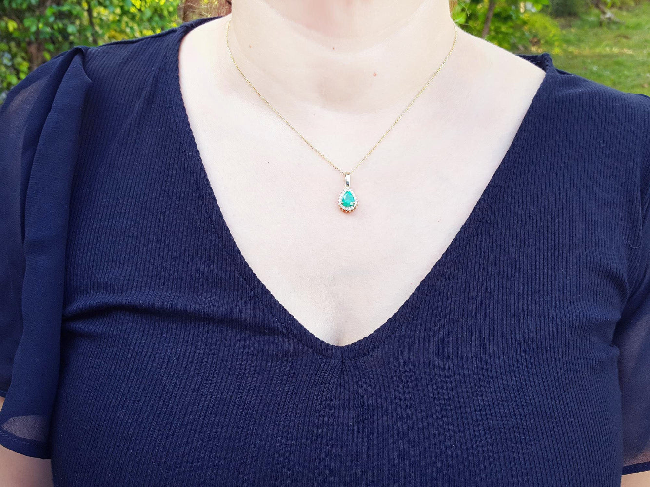 Navy blue dress with a colombian emerald pendant necklace on a woman against a blurred green outdoor background.