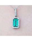 White gold emerald pendant with diamond accents on a light pink skin background.