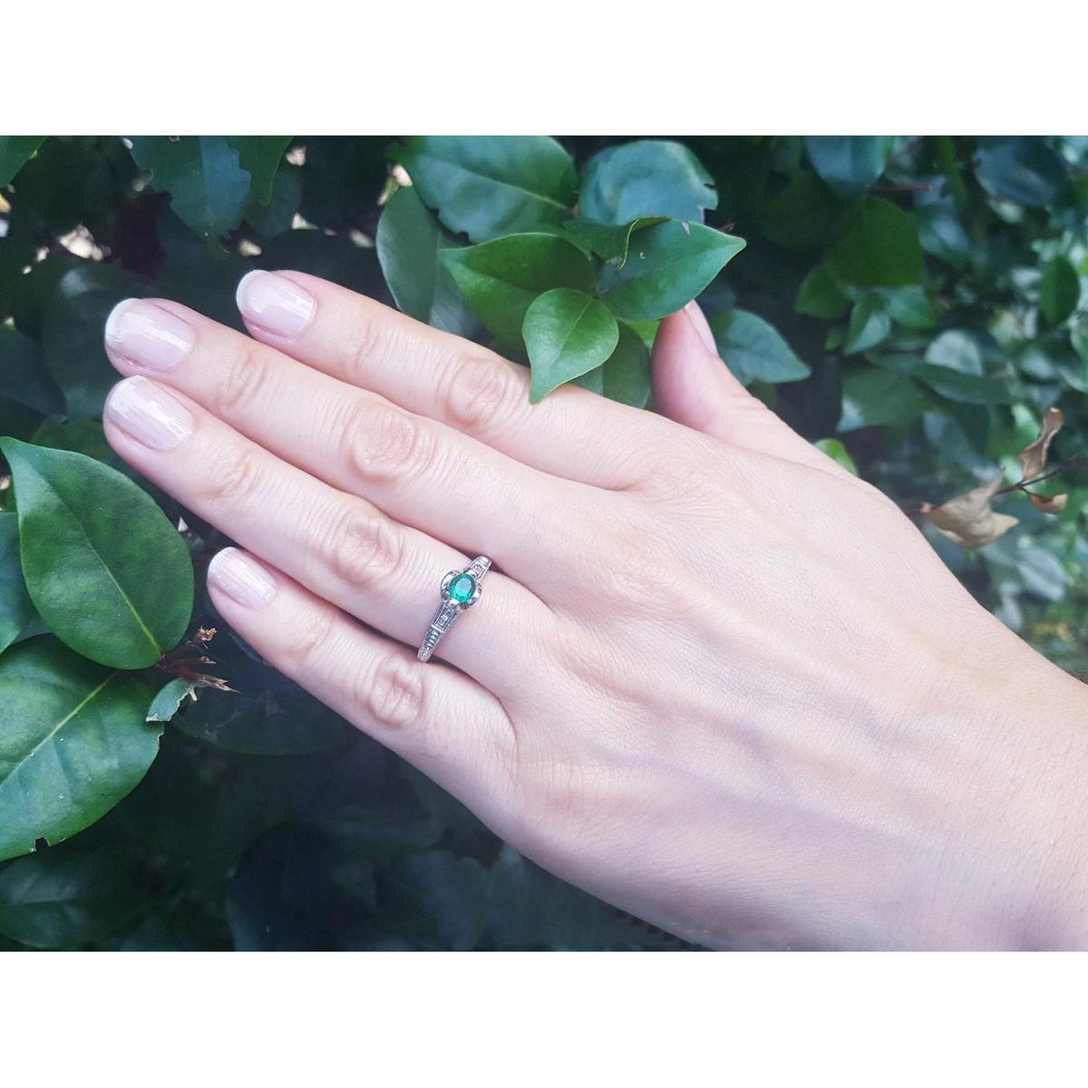 Hand wearing a natural oval cut colombian emerald ring against a leafy background.