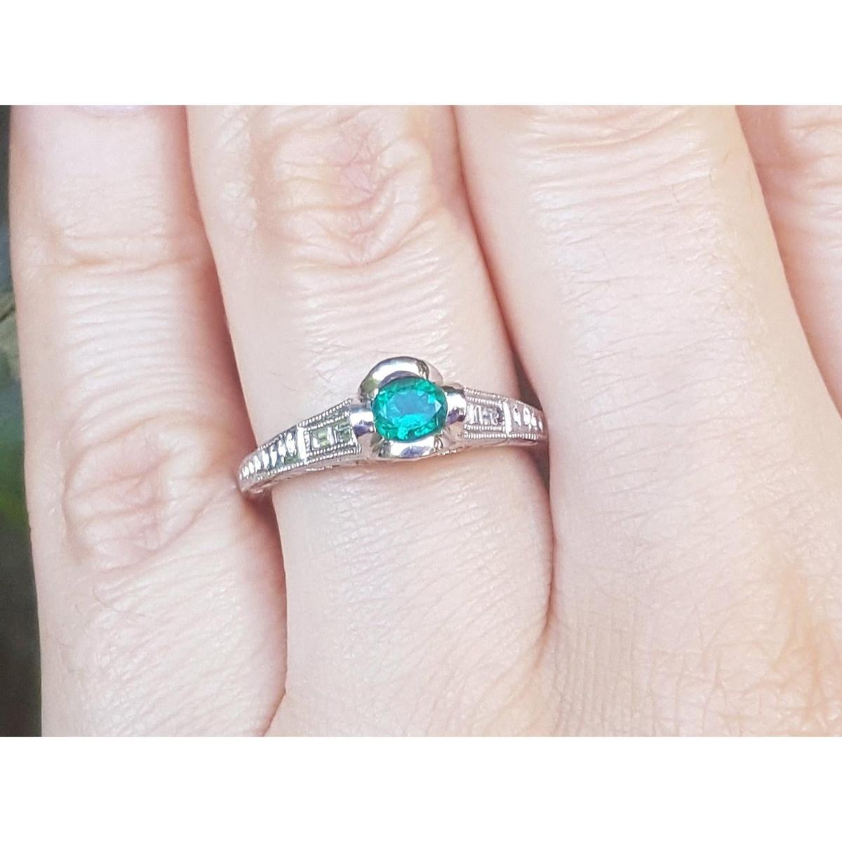 A natural oval cut colombian emerald ring in white gold on a finger.