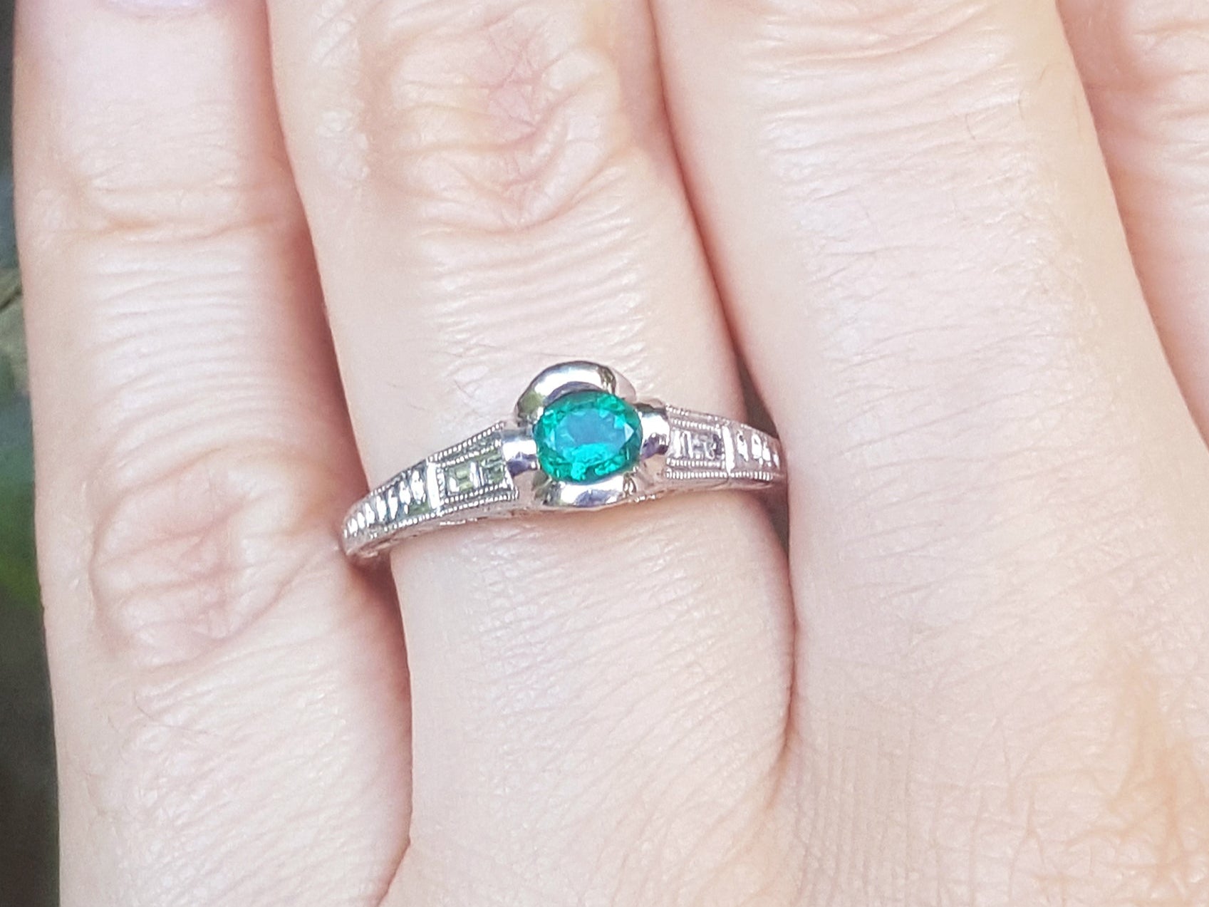 A natural oval cut colombian emerald ring in white gold on a finger.