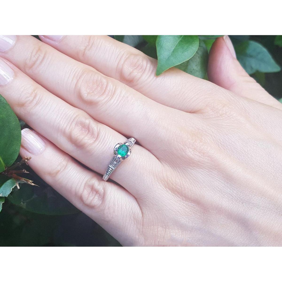Hand wearing a ring with a colombian emerald against a natural background.