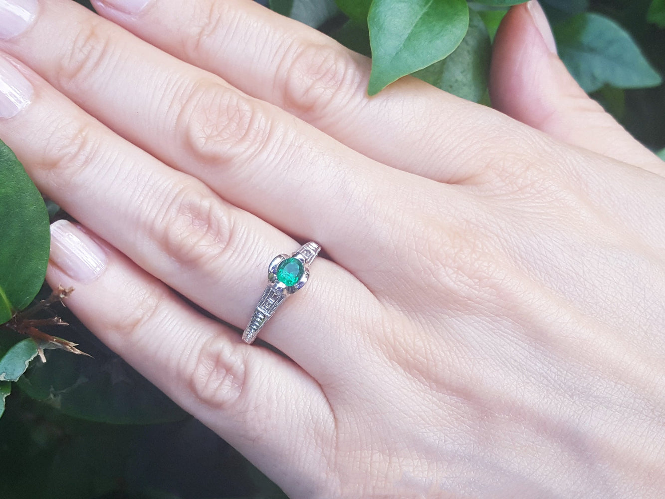 Hand wearing a ring with a colombian emerald against a natural background.