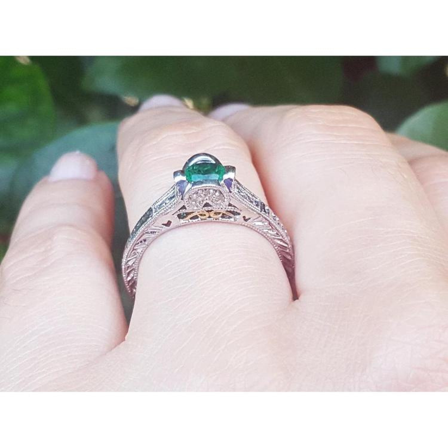 Oval Colombian emerald ring with baguette diamonds in engraved 14K white gold on a hand.
