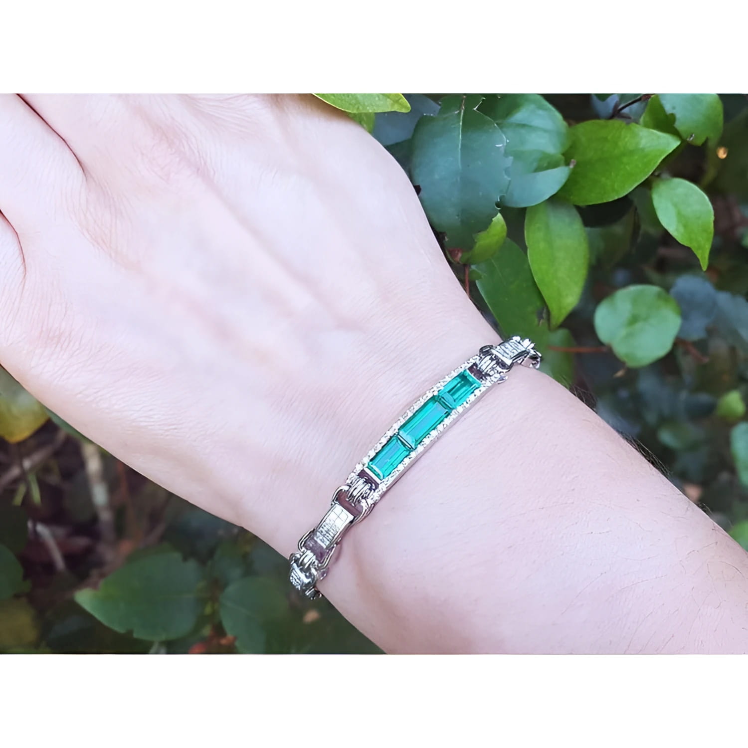 Silver bracelet with vibrant Colombian emeralds and princess cut diamonds on a wrist.