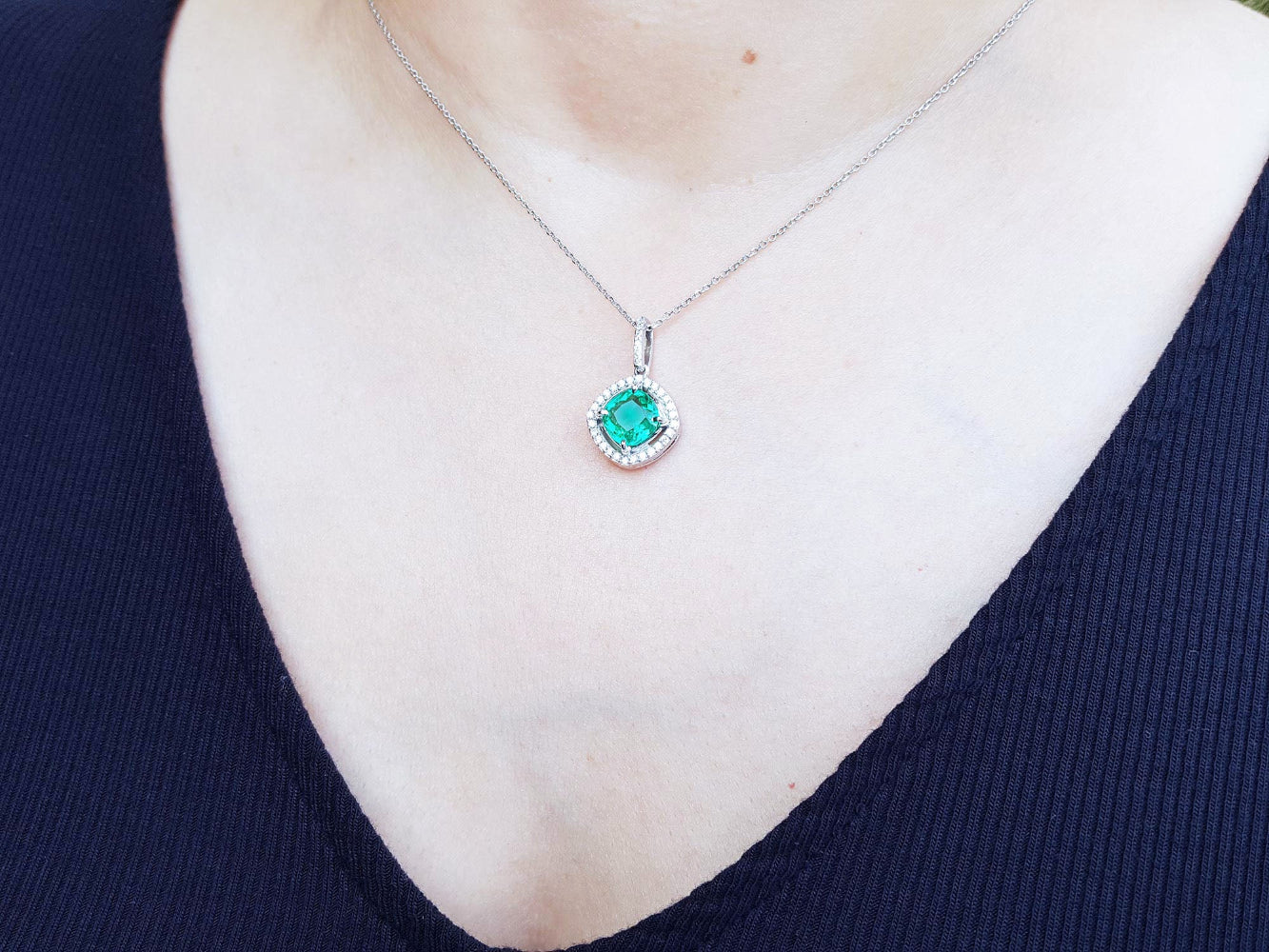 Close-up of a necklace with an emerald gemstone pendant on a person wearing a dark blue top.