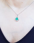 Close-up of a necklace with an emerald gemstone pendant on a person wearing a dark blue top.