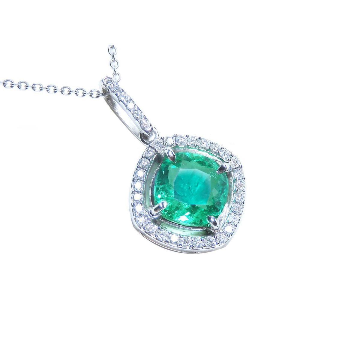 A cushion cut emerald gemstone pendant with diamond halo on a topside view.