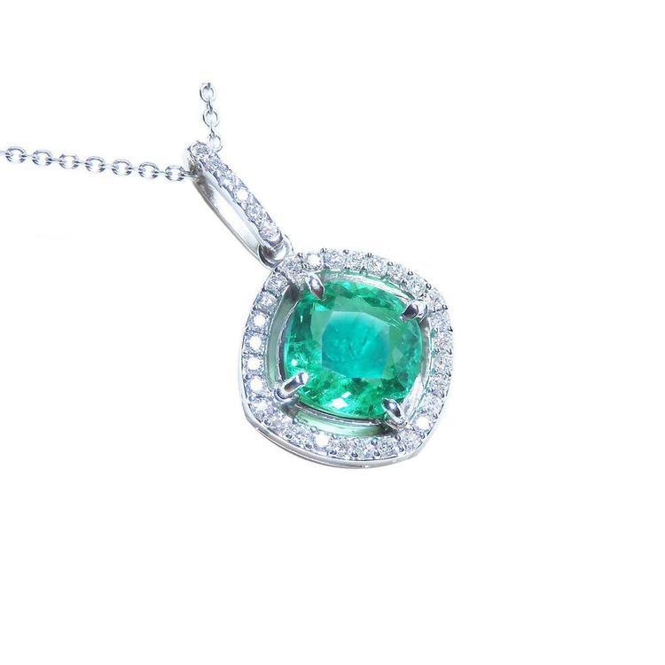A cushion cut emerald gemstone pendant with diamond halo on a topside view.
