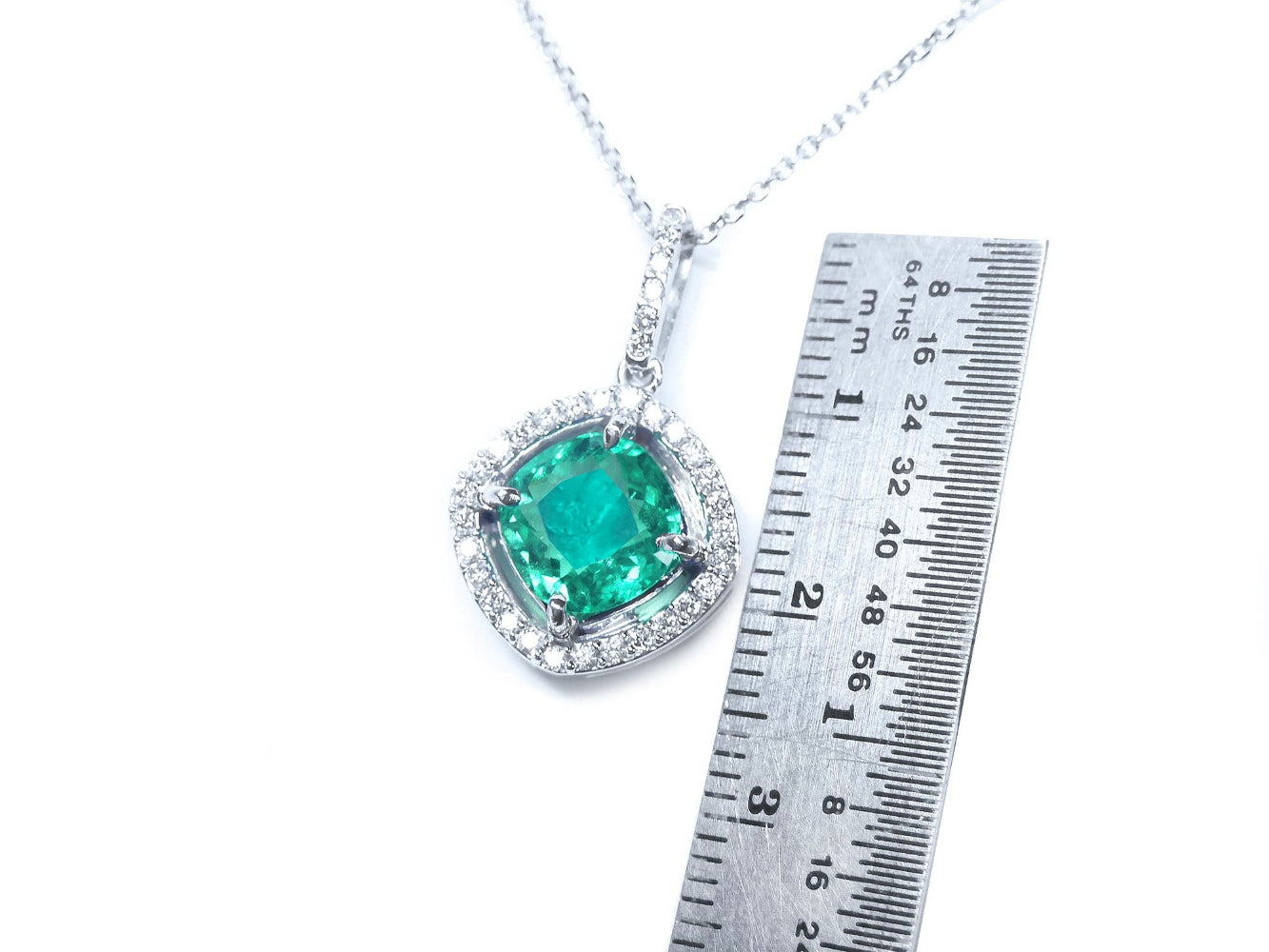 Emerald pendant on a white gold chain with a ruler for scale on a white background.