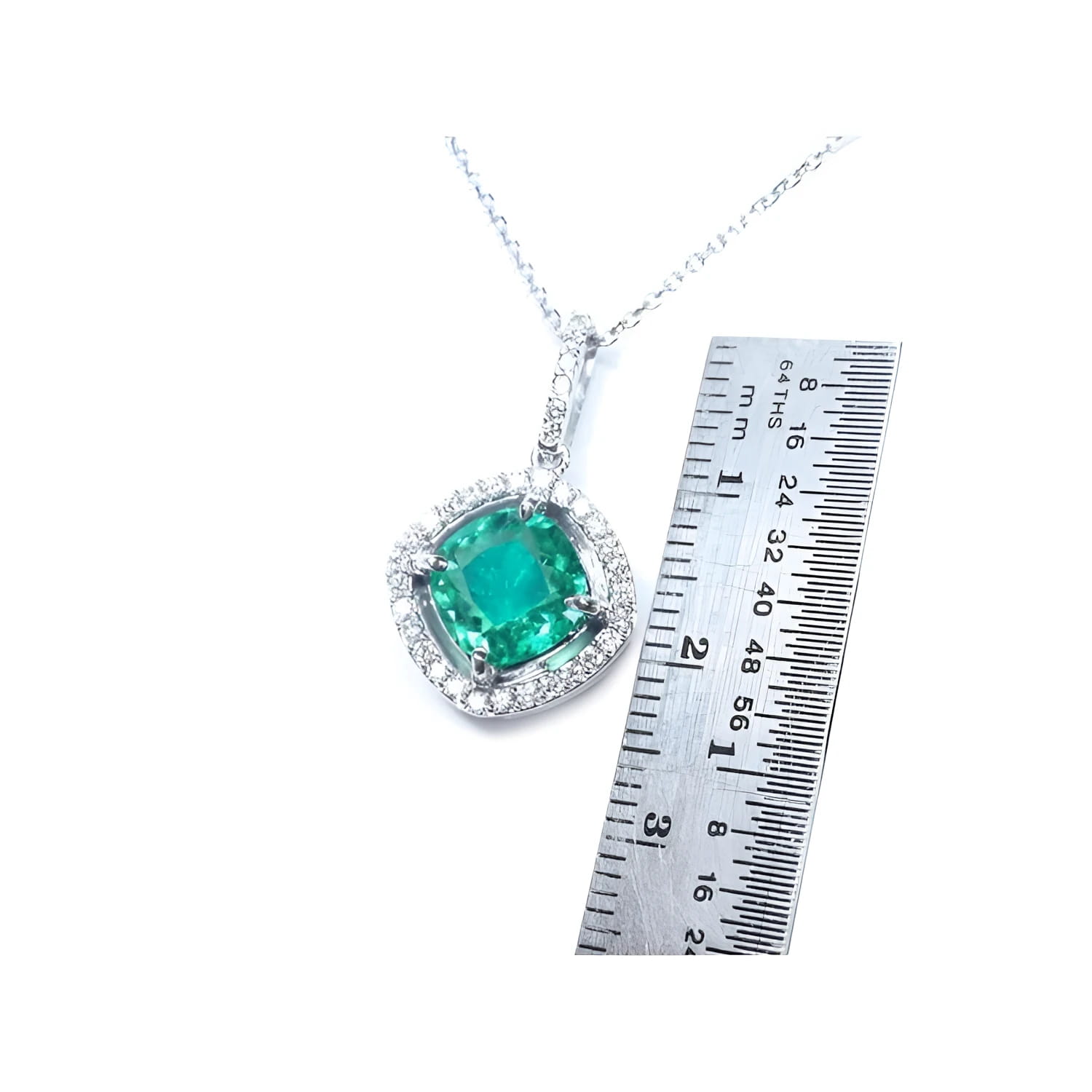 Cushion-cut Colombian emerald pendant with halo diamonds in 14K white gold, next to a ruler.