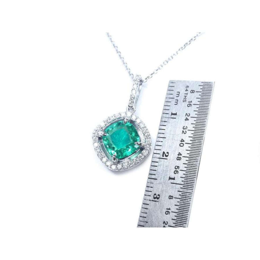 Cushion-cut Colombian emerald pendant with halo diamonds in 14K white gold, next to a ruler.