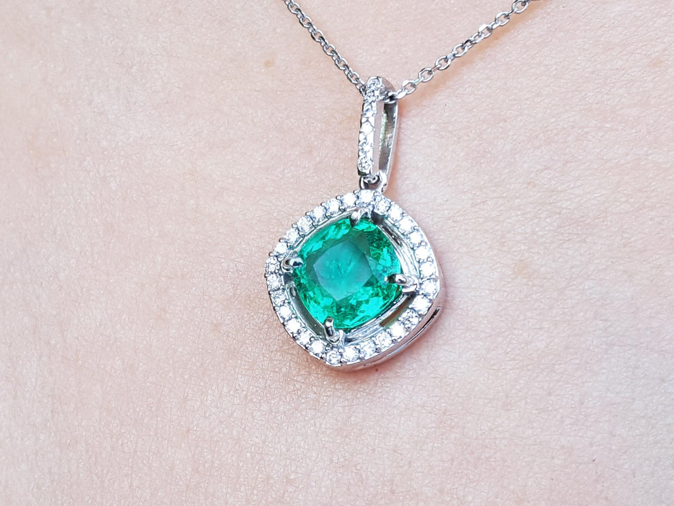 Emerald pendant with diamond accents on a light pink skin background.