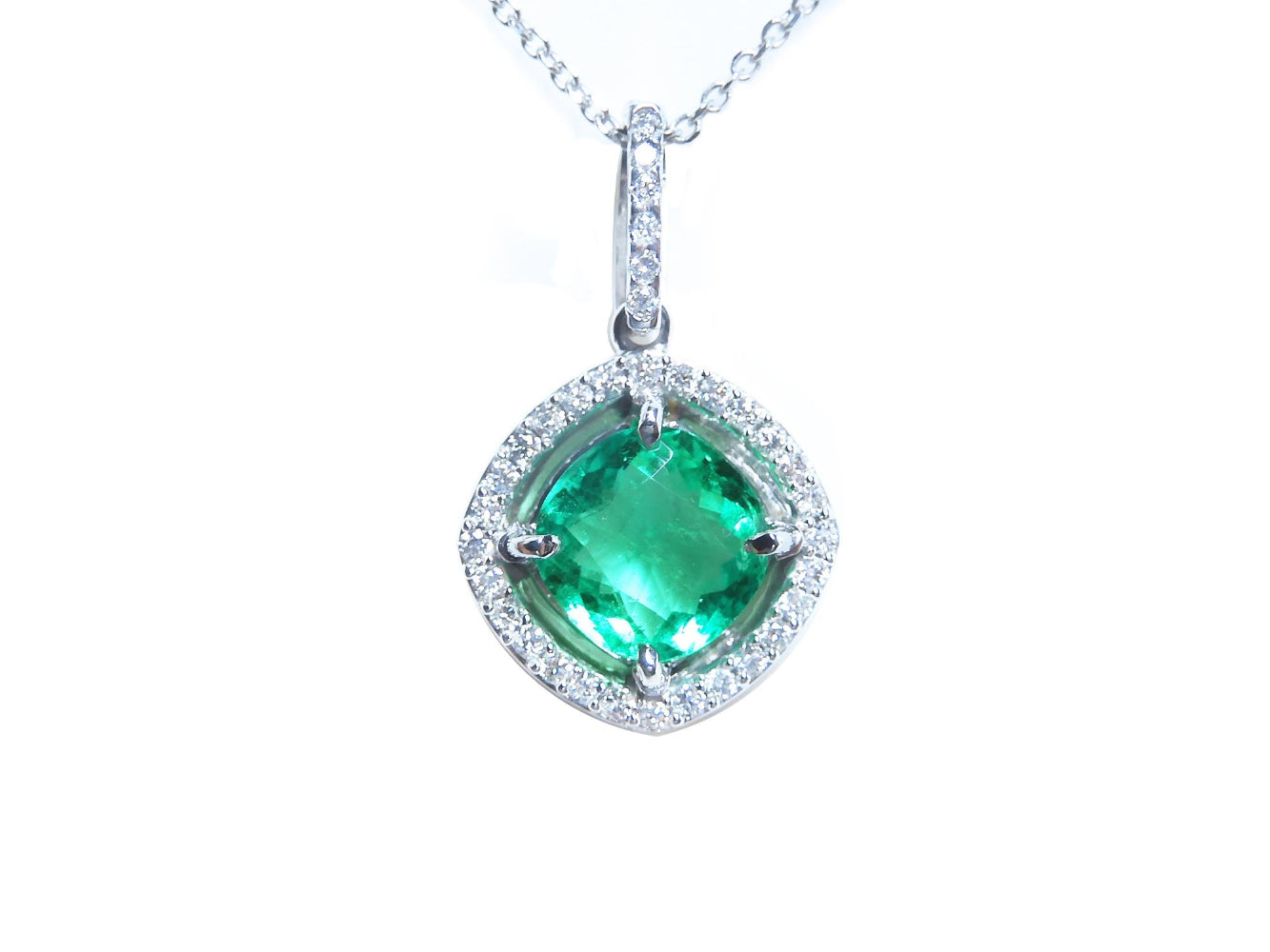 Emerald cushion cut with halo diamond pendant necklace on a topside view.