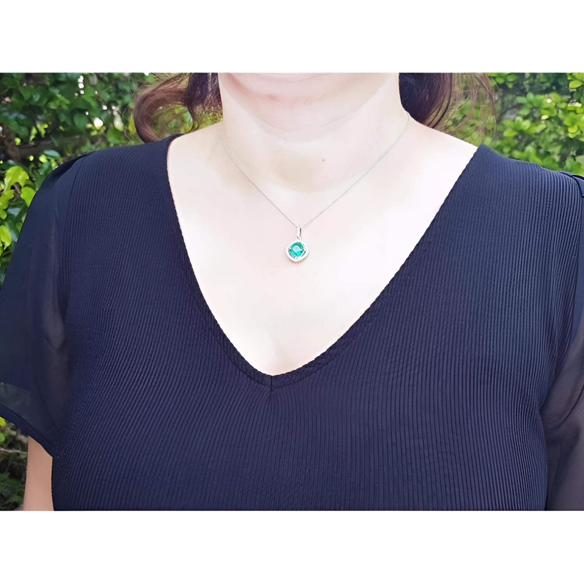 Cushion-cut Colombian emerald pendant with halo diamonds on a 14K white gold chain, worn on a woman.