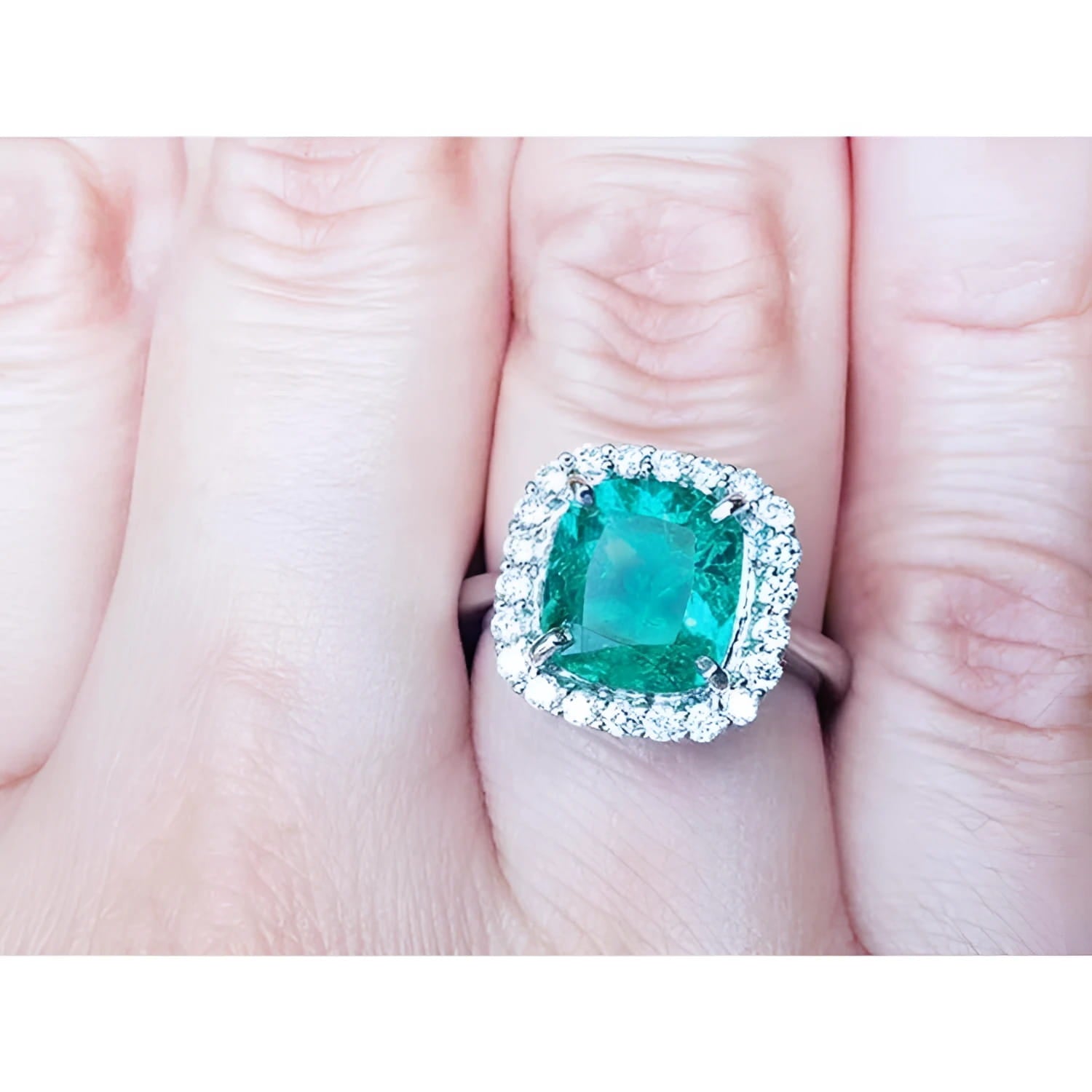 An emerald engagement ring cushion cut with a halo of natural diamond in white gold on a finger.