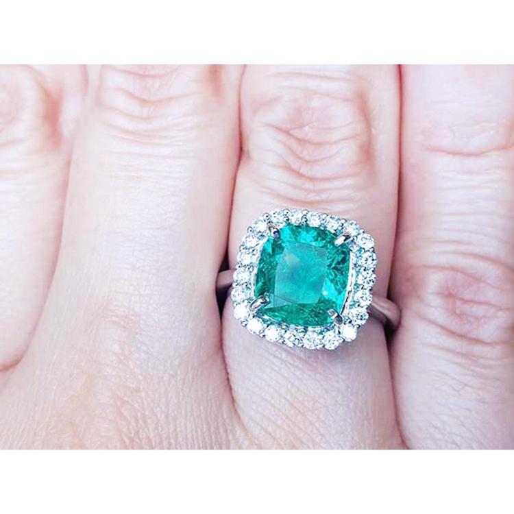 An emerald engagement ring cushion cut with a halo of natural diamond in white gold on a finger.