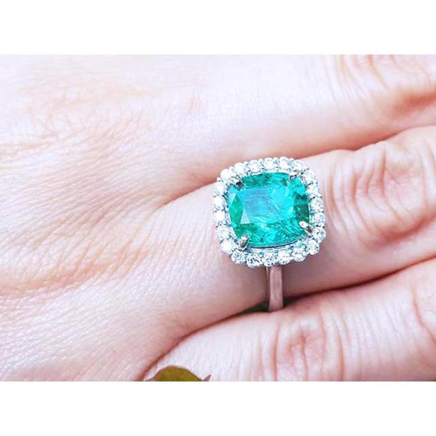 Cushion cut Colombian emerald ring with diamond halo on 18K white gold band.
