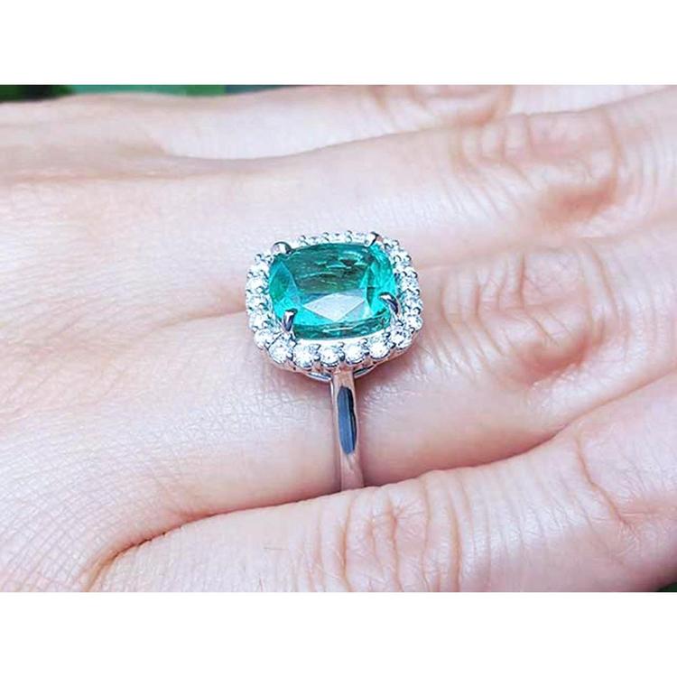 Cushion cut Colombian emerald ring with diamond halo in 18K white gold on a hand.