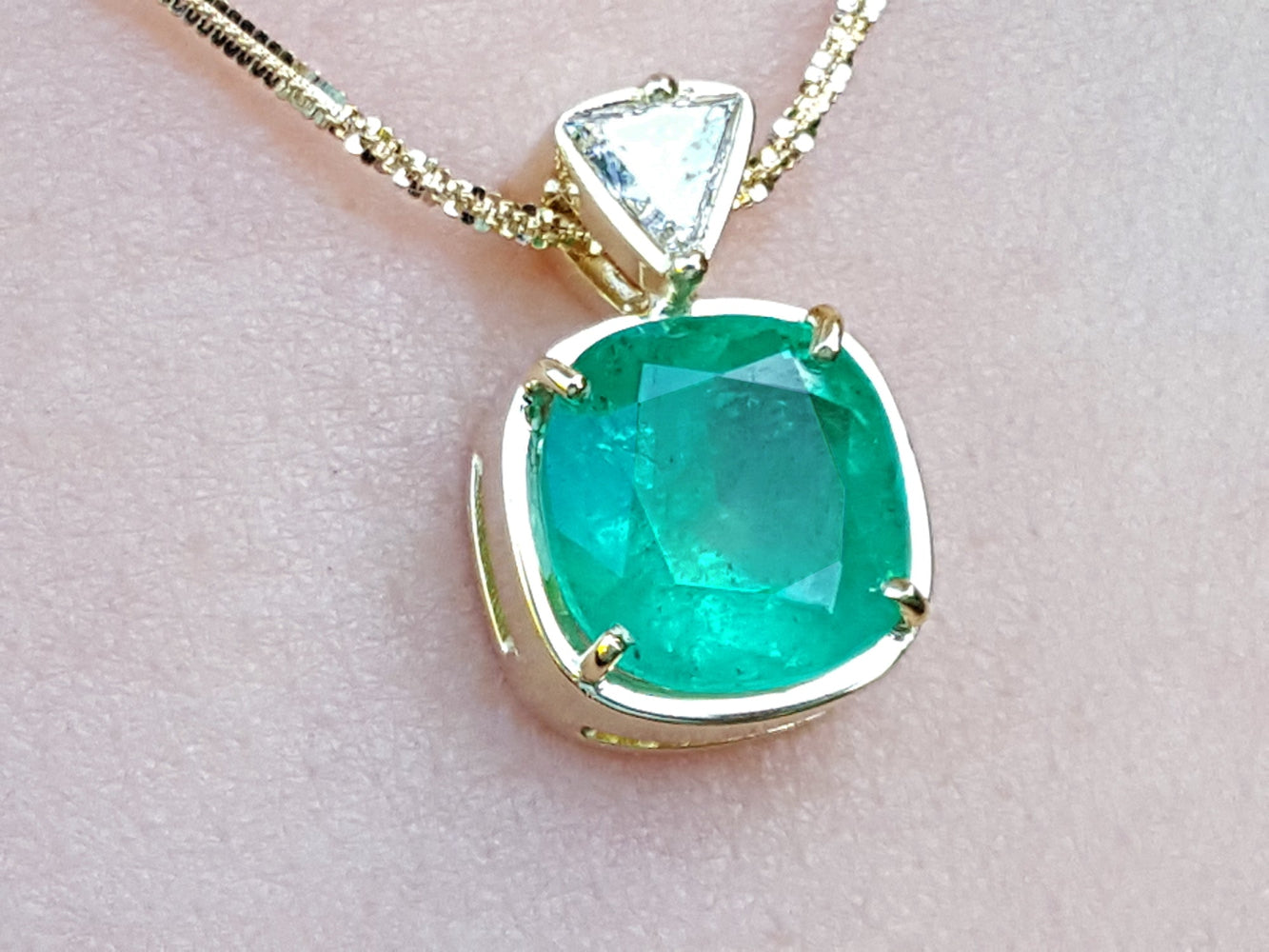 A genuine colombian emerald pendant with gold setting on a light skin background