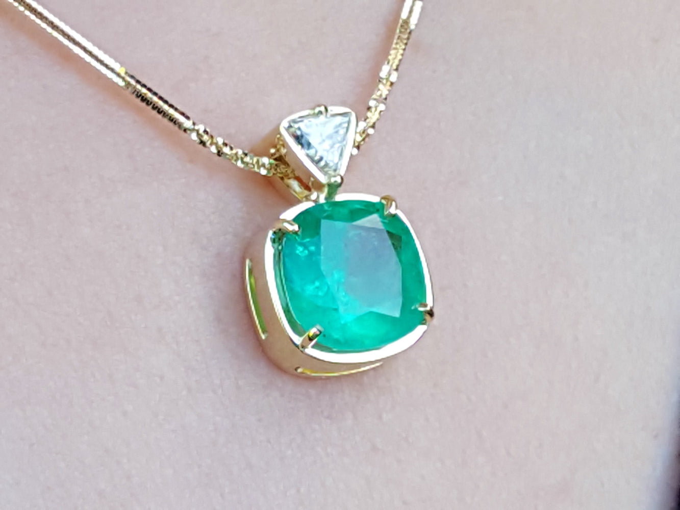 Gold necklace with a Muzo colombian emerald pendant on a light skin background