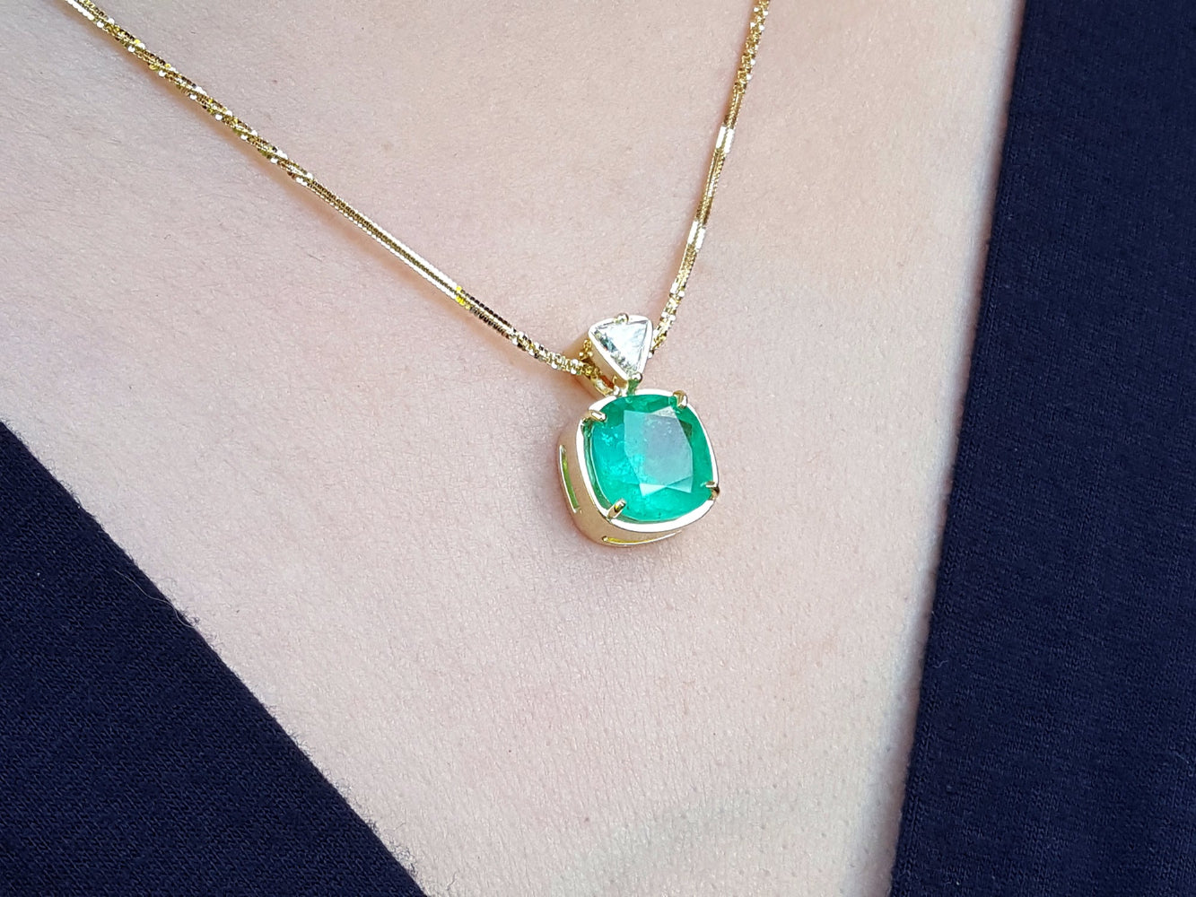 Gold necklace with a cushion cut emerald pendant on a person&#39;s neck