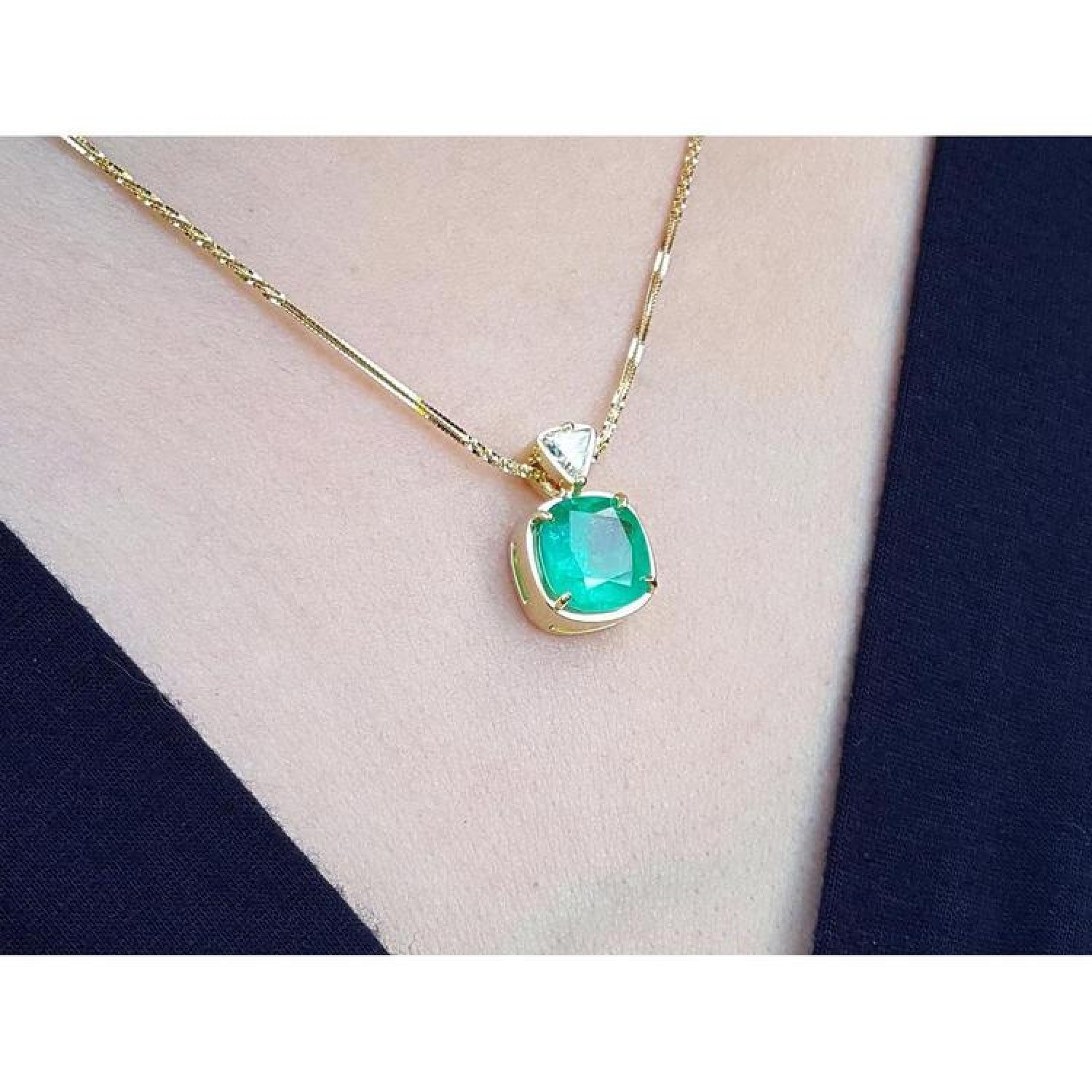 Cushion cut emerald pendant necklace in 18K yellow gold, worn on a person.