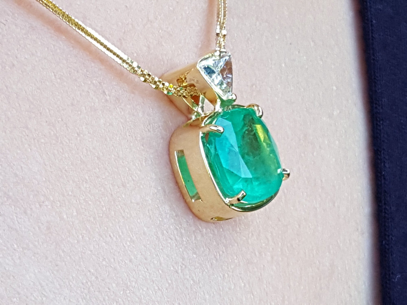 Gold pendant with a natural cushion cut colombian emerald on a light skin background