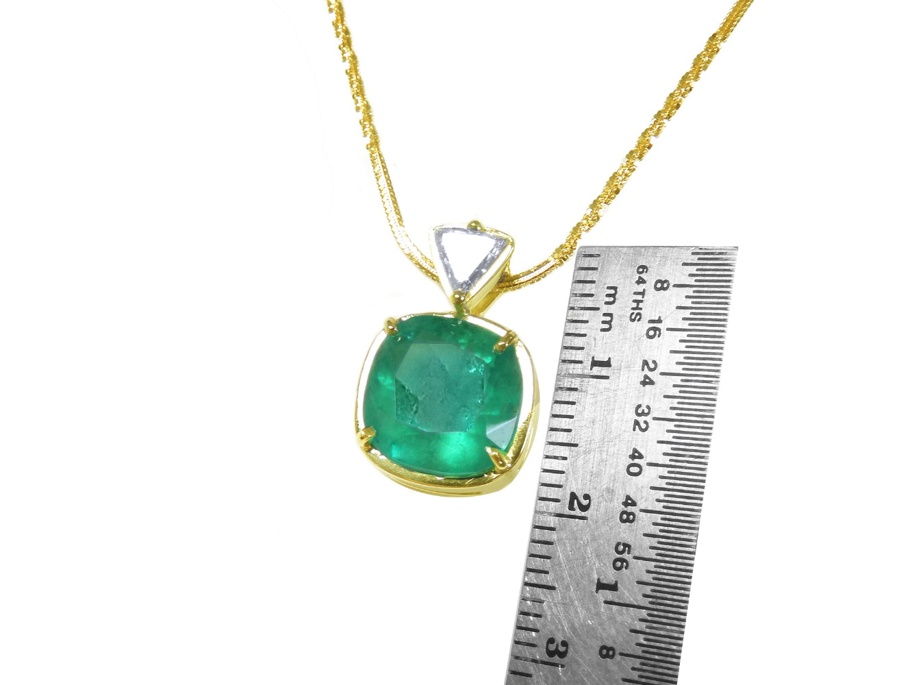 Gold pendant with a cushion cut colombian emerald next to a ruler on a white background