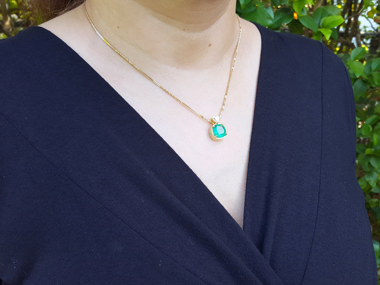 Person wearing a gold necklace with a colombian emerald pendant against a natural background