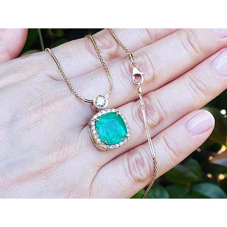 Cushion cut halo diamonds gold necklace held in a hand against a blurred natural background