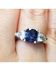 14k white gold ring with a blue cushion cut natural sapphire and two triangular sapphires on a finger.