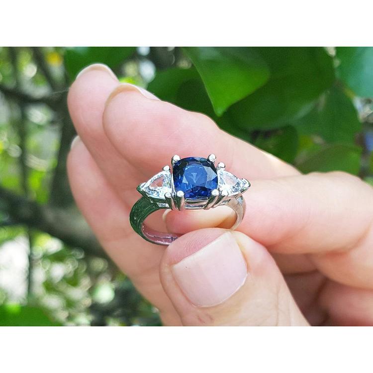 Cushion cut deep blue sapphire ring with trillion side sapphires in white gold.
