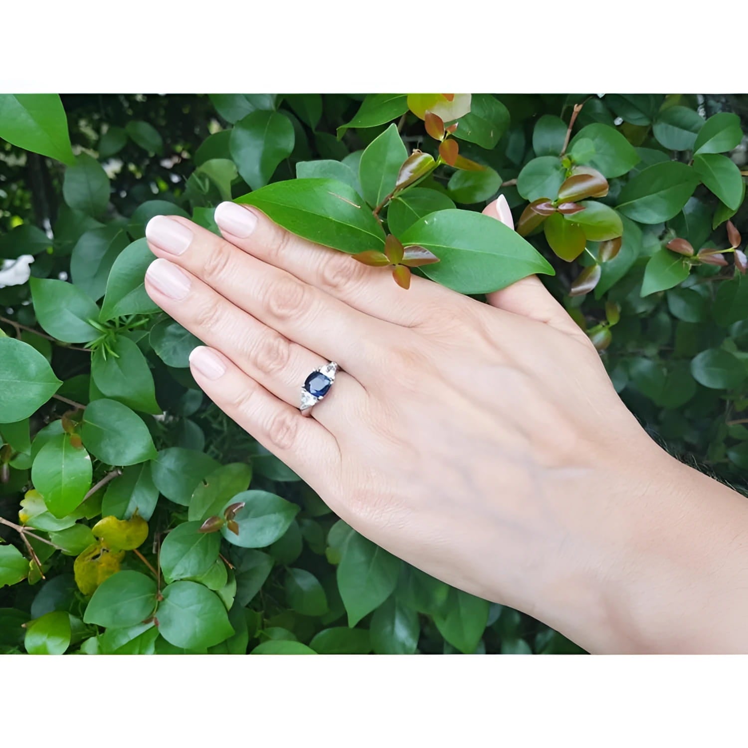Cushion cut deep blue sapphire ring with trillion side sapphires in 14K white gold on a hand.