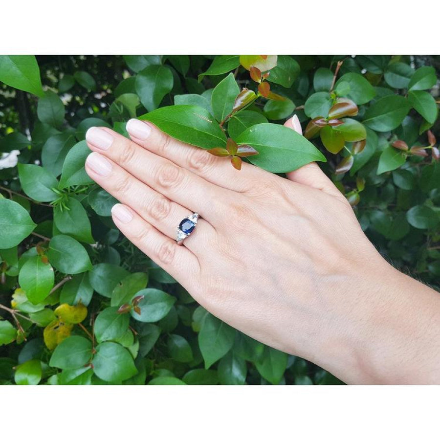 Cushion cut deep blue sapphire ring with trillion side sapphires in 14K white gold on a hand.
