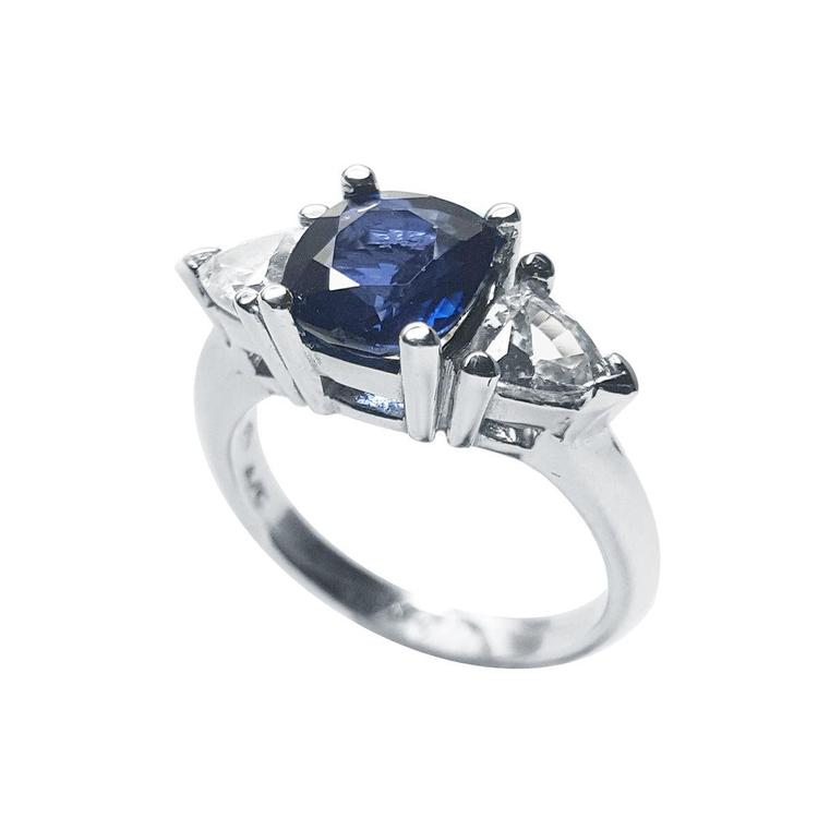 Deep blue cushion cut sapphire ring with trillion side sapphires in white gold.